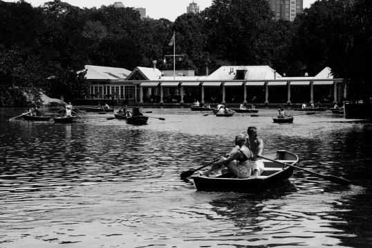 Fit couple in foreground enjoy leisurely paddle on the Lake in Central Park